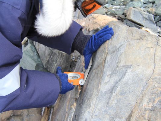 De richting van de foliatie wordt nagegaan met een geologisch kompas.